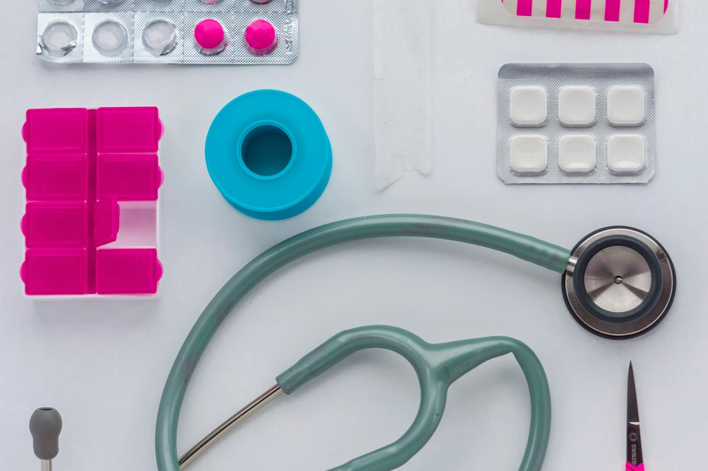 A green and black stethoscope beside pill organisers on white paper