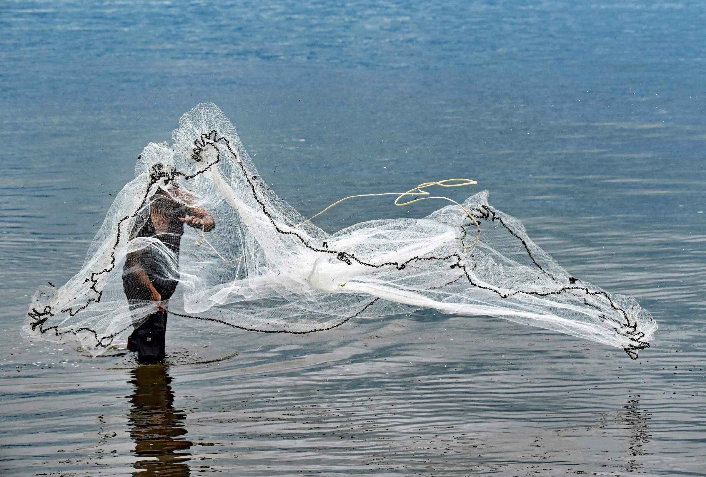 A person throwing a white fishing net across open water